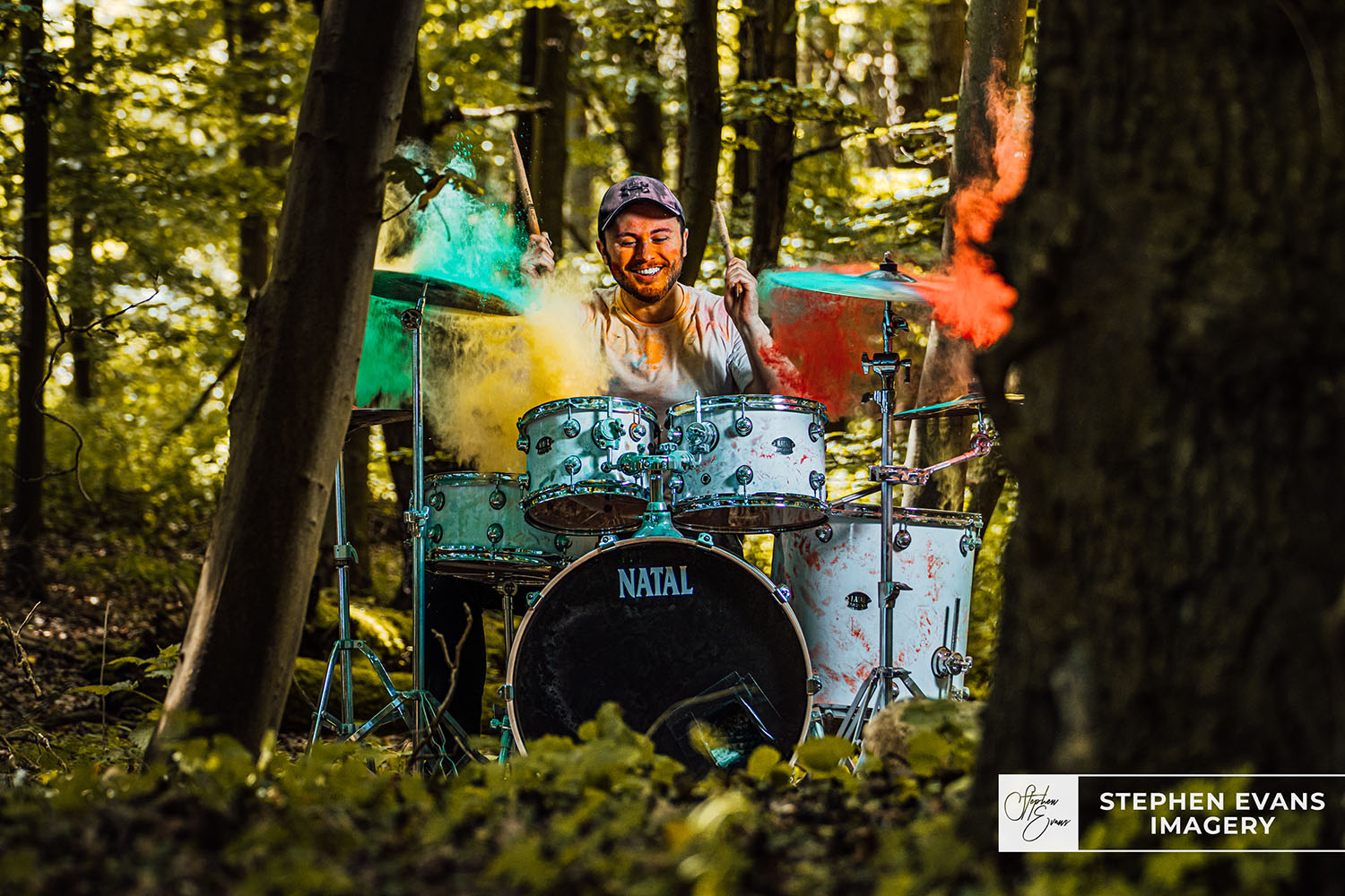 Drummer Joe playing white drum kit with paint powder explosion in forest
